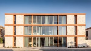 Façade contemporaine méditerranéenne en pierre claire, dotée de grandes fenêtres à double vitrage baignées par la lumière douce de l’hiver.
