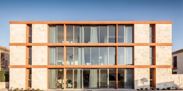 Façade contemporaine méditerranéenne en pierre claire, dotée de grandes fenêtres à double vitrage baignées par la lumière douce de l’hiver.