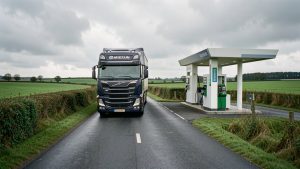 Camion poids lourd moderne roulant sur une route rurale bretonne près d’une station de biogaz, avec des champs verdoyants et un ciel nuageux.